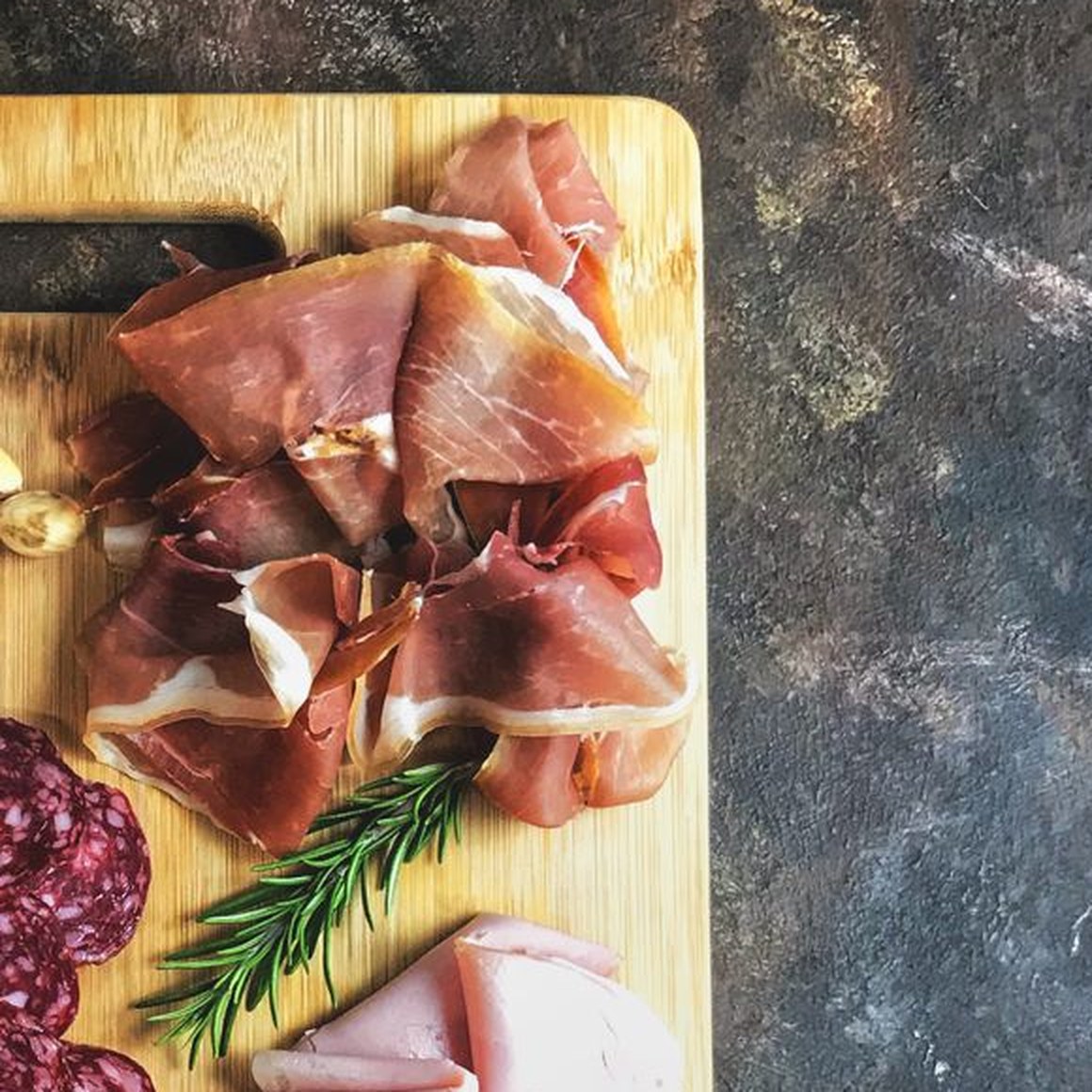 Folds of thinly sliced prosciutto on a wooden board